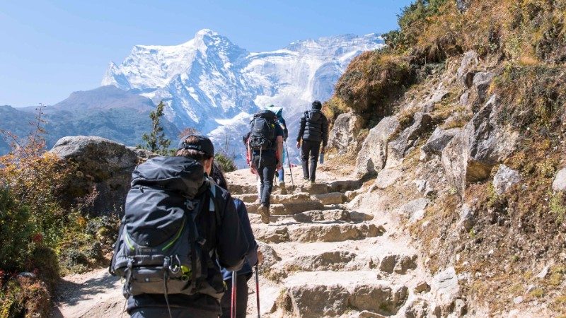 Three travellers with backpacks hiking up stars with mountain peaks in the distance 