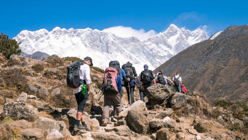 Group of travellers hiking along stairs to reach Everest Base Camp. White snowy peaks are seen in the distance.