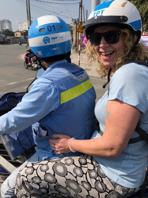 A smiling woman on the back of a motorbike