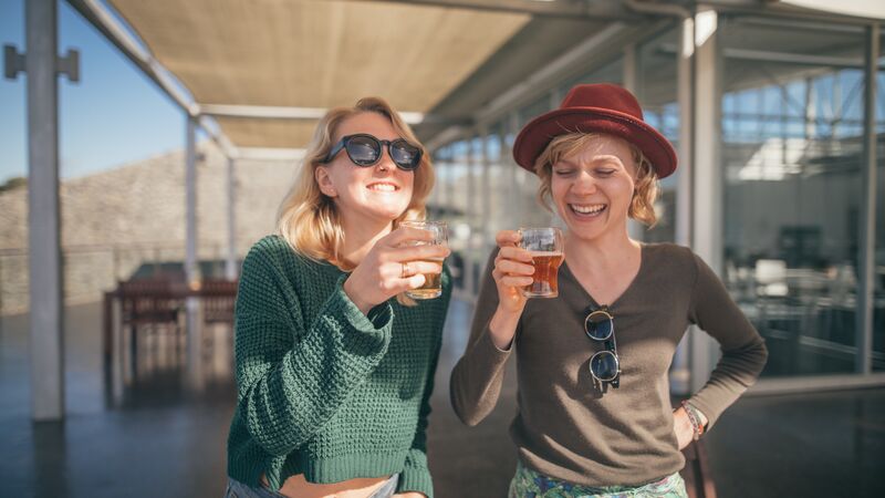 Two women smiling while holding glasses of beers in a brewery.