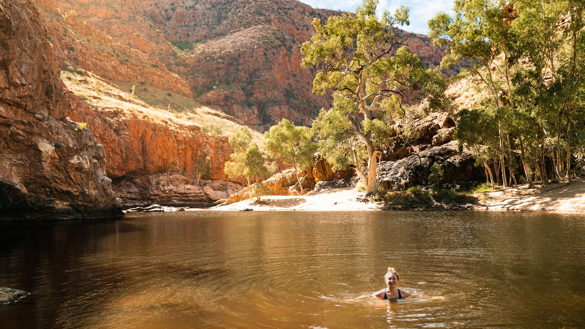 A woman smiles to camera while swimming in Ormiston Gorge.