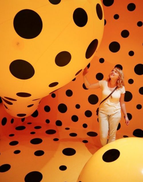 A woman surrounded by enormous orange balls in a gallery.