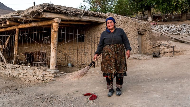 Uzbek woman stands in front of her village home with a broom.