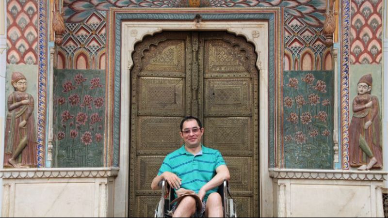 A man in a wheelchair sits in front of an ornate door at a palace