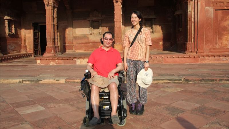 A man sits in a wheelchair next to a young woman in India.