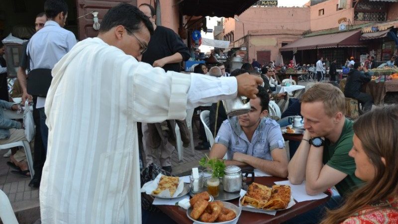 A man pouring tea and local treats for travellers in Marrakesh.