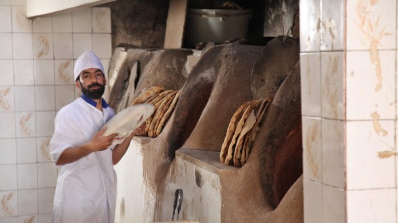A baker loading bread into an oven