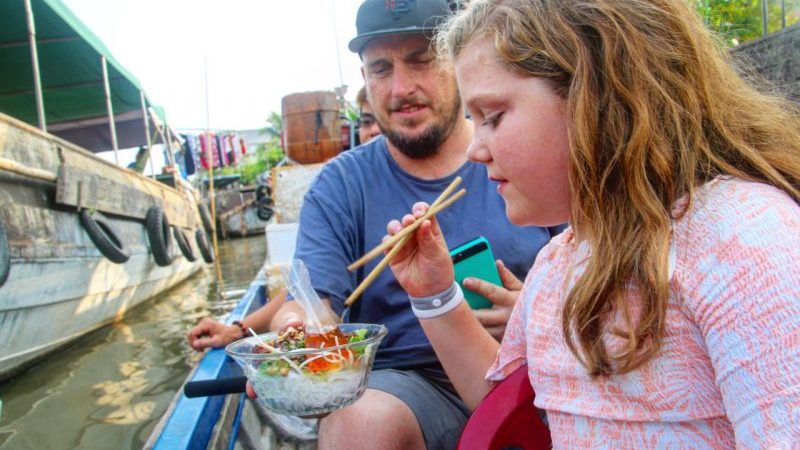 A girl and her dad eating noodles on a boat