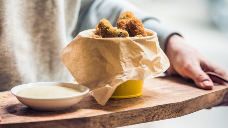 Person holding a wooden tray with a bucket of fried pickles on it