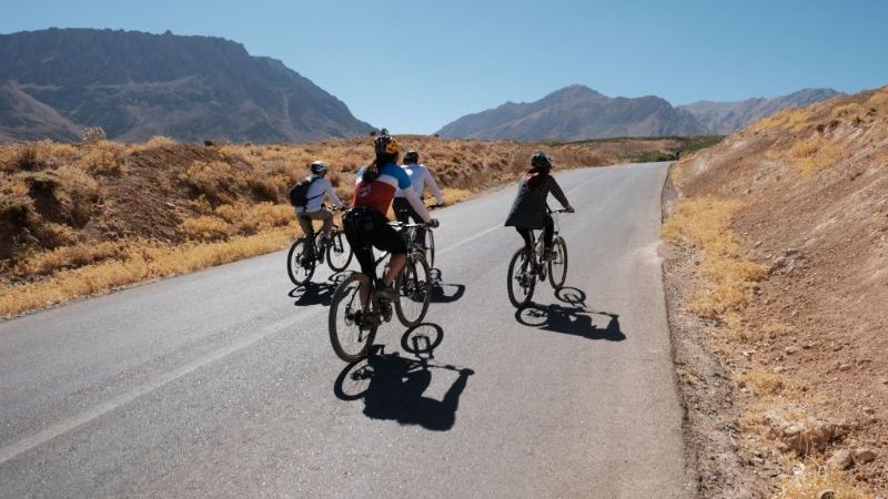 A group of cyclists ride down a quiet road in Iran