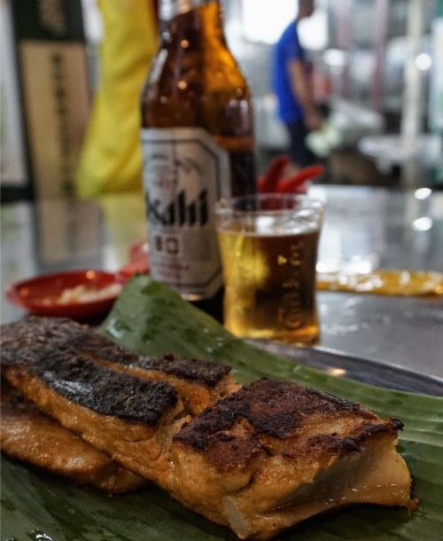 Grilled fish on a banana leaf and a beer in the background