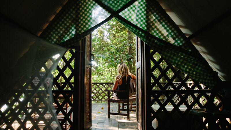 A woman sitting on a porch outside a jungle hut