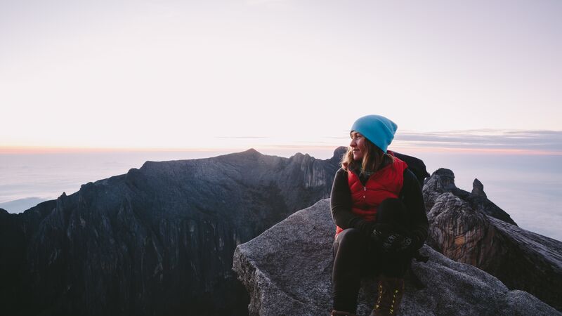 A woman wearing a blue beanie on the top of a mountain