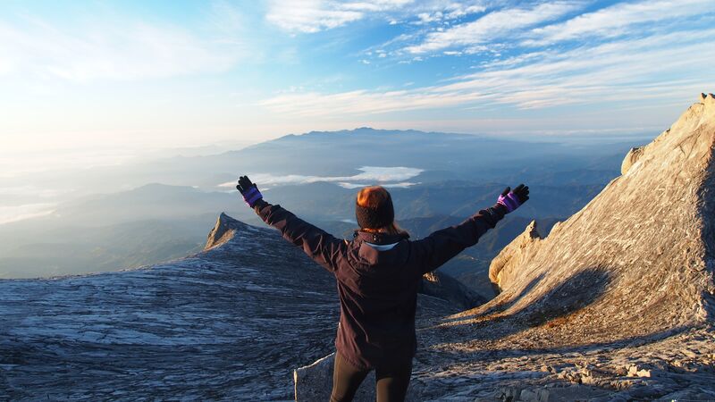 A woman stands with her arms in the air on the top of Mt Kinabalu