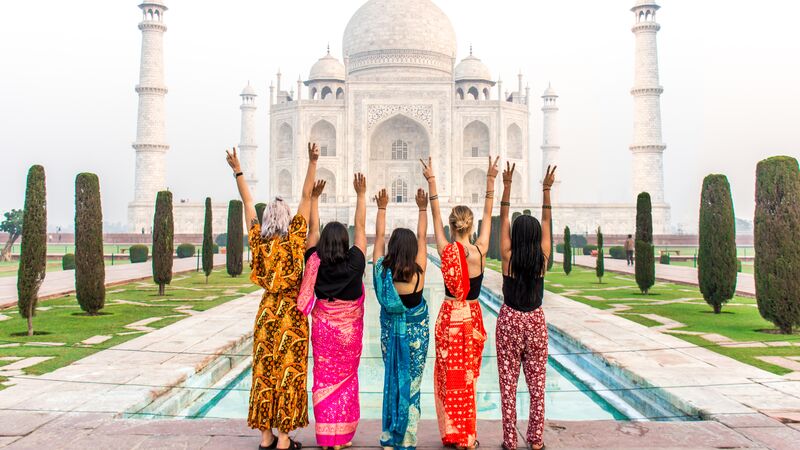 Five woman facing the Taj Mahal with their arms up