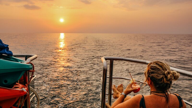 A traveller in Thailand watches the sunset with a cocktail from the deck of the boat.