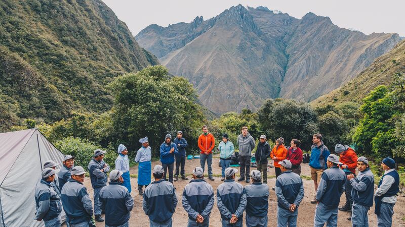 A group of porters, travellers and guides stand in a circle on the Inca Trail