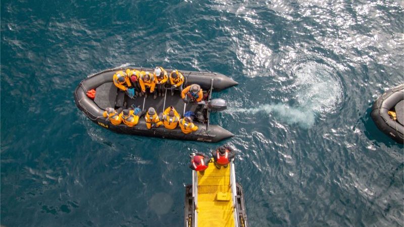 Aerial view of passengers in a Zodiac and a yellow gangway with two people on it