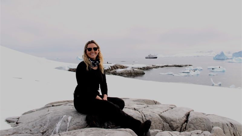 A woman wearing black sitting on a rock in the snow