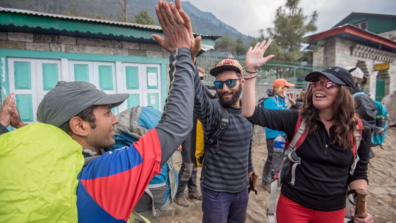 Two hikers high-fiving a local in Nepal.