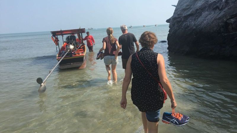 Three people wading through water to board a boat