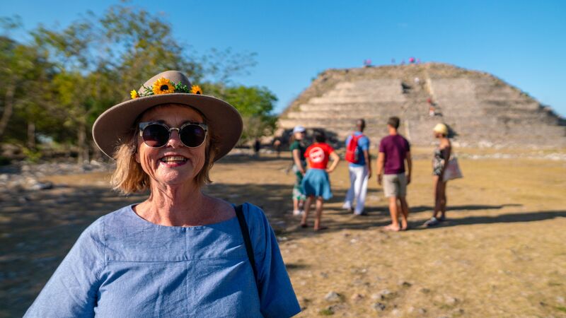 A woman in a blue shirt and a hat in front of a pyramid in mexico