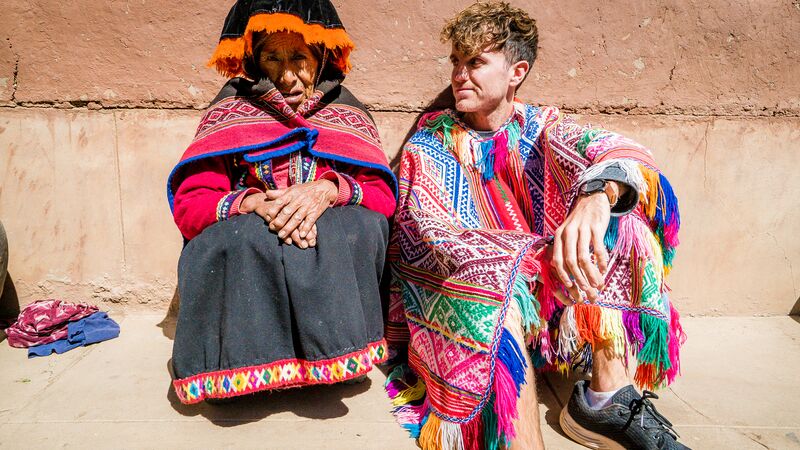 A young traveller in a traditional Peruvian costume sitting next to a local woman