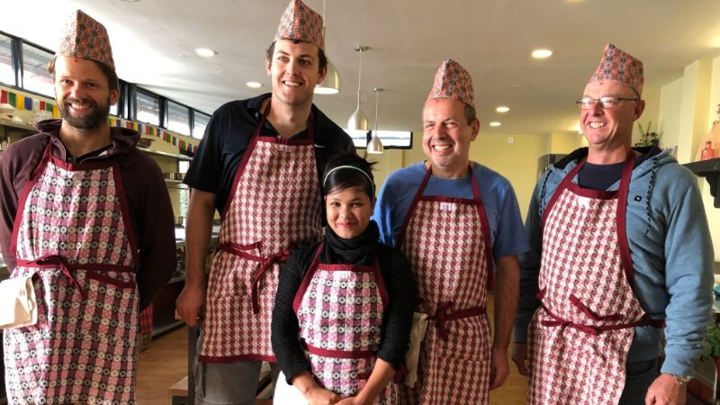 Four men and a women wearing red and white checked aprons