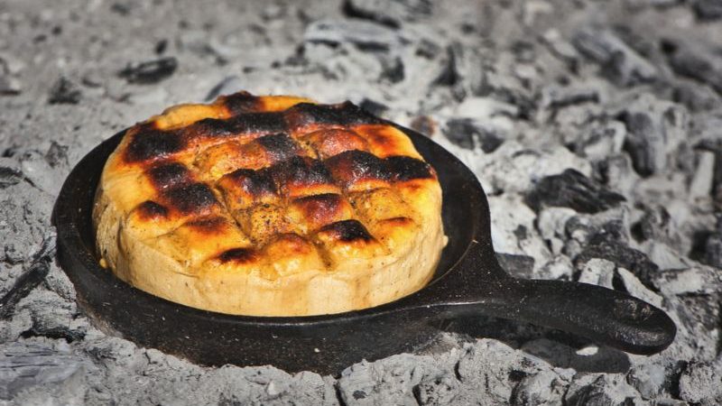 A small skillet of cheese sitting in a coal pit