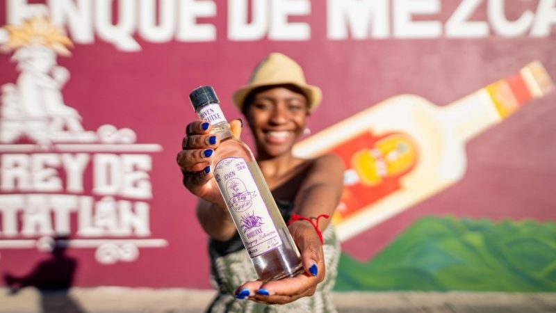 A young woman holds up a bottle of mezcal in Mexico