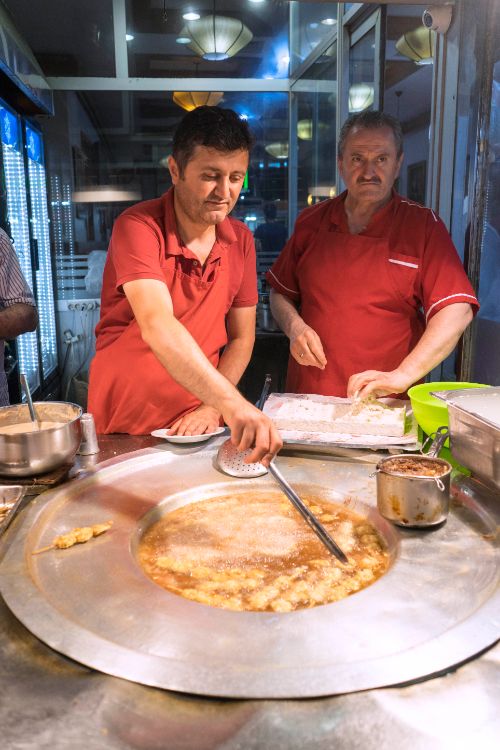 Two men stirring a vat of mussels in oil at a market