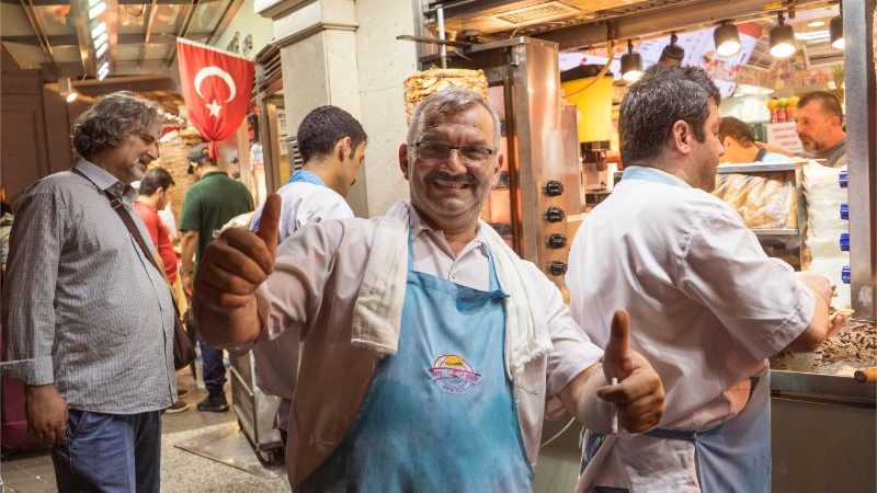 A man in a busy market giving a thumbs up to the camera