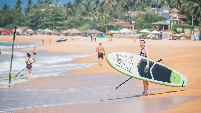 A woman on the beach holding a standup paddle board