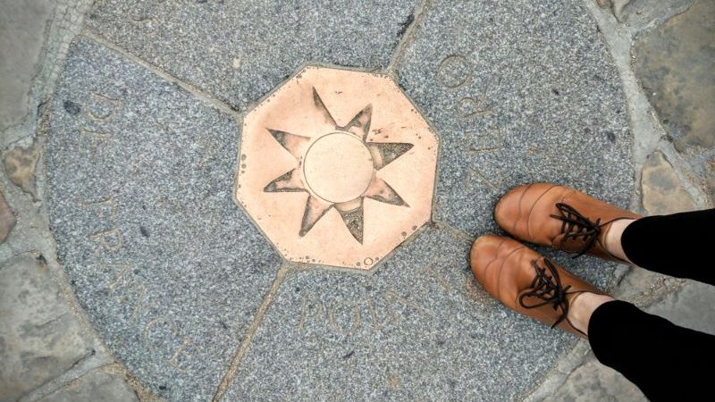 The bronze plaque at Point Zero, with a persons shoes.