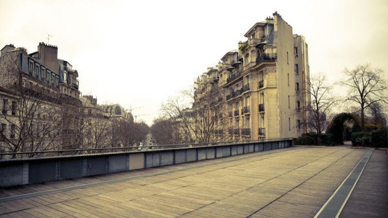 An old railway line, now a walking path, with French apartments in the background