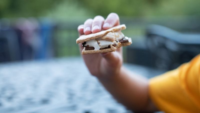 A person in a yellow tshirt holding up a smore. 