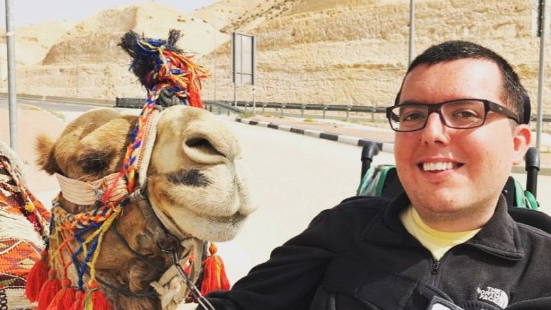 A smiling man sitting beside a camel