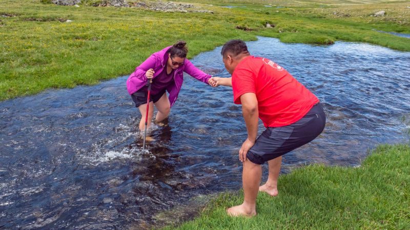 A man helps a woman across a stream