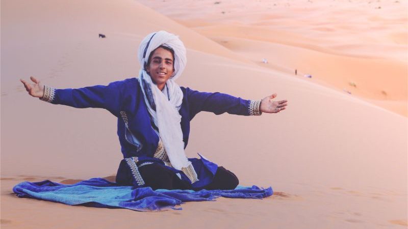 A Berber wearing blue sitting on the sand in the desert