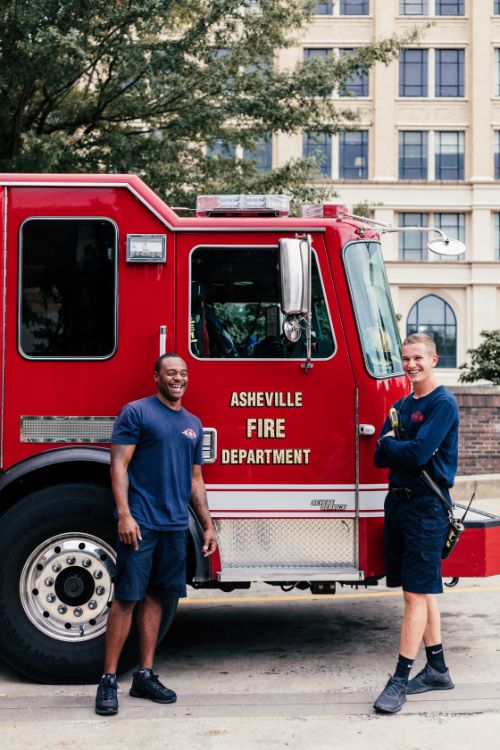 Two firefighters posing alongside their truck