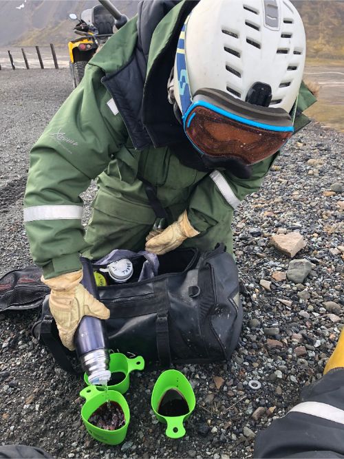 A person wearing snow gear in the Arctic filling up cups with juice