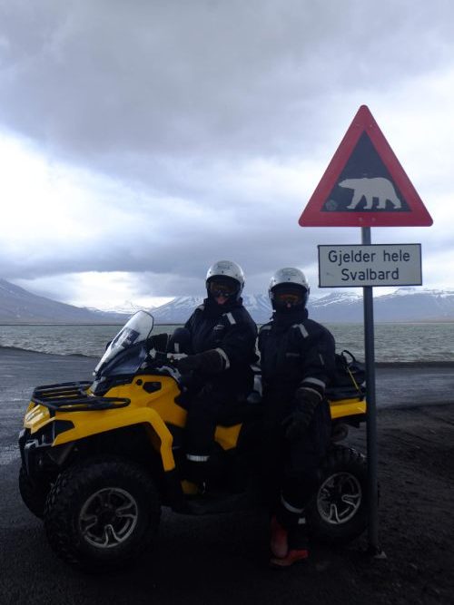 Two people on an ATV in front on a polar bear sign