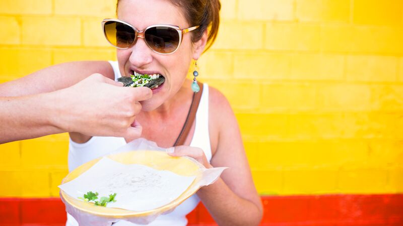 A woman eating a taco in front of a colourful wall
