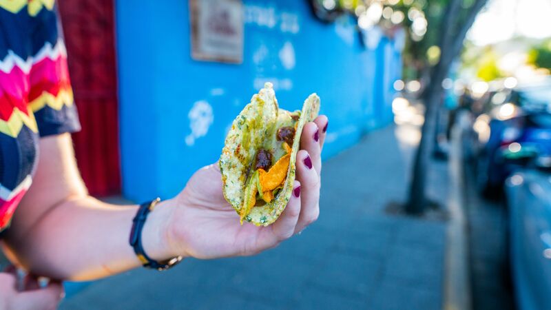 A woman holding a taco in front of a blue wall in Mexico