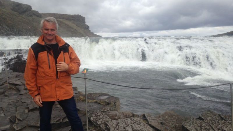 A man in a yellow jacket at a waterfall in Iceland