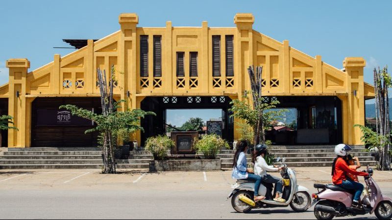 A yellow building with motorbikes riding past