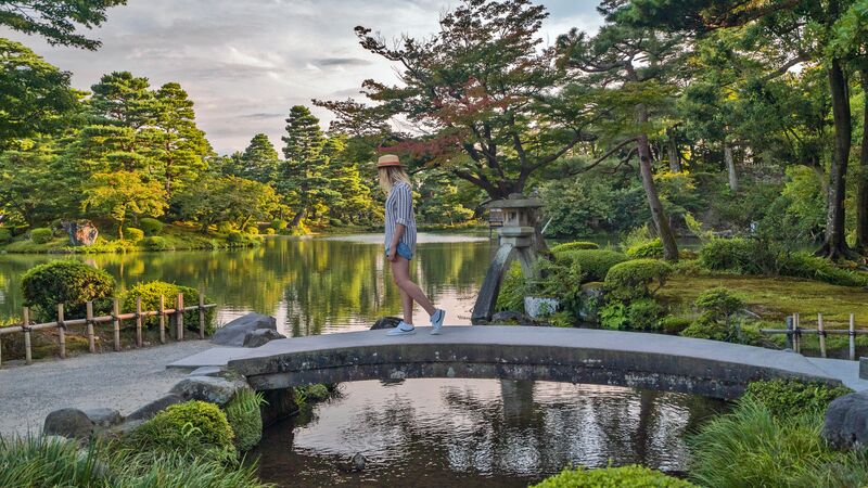 A young woman crosses a bridge in a tranquil park in Japan