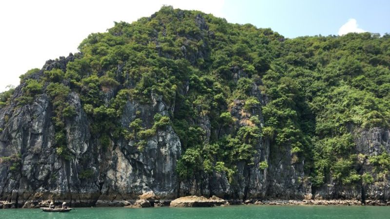 two people in a small boat cruising past a limestone karst in Vietnam