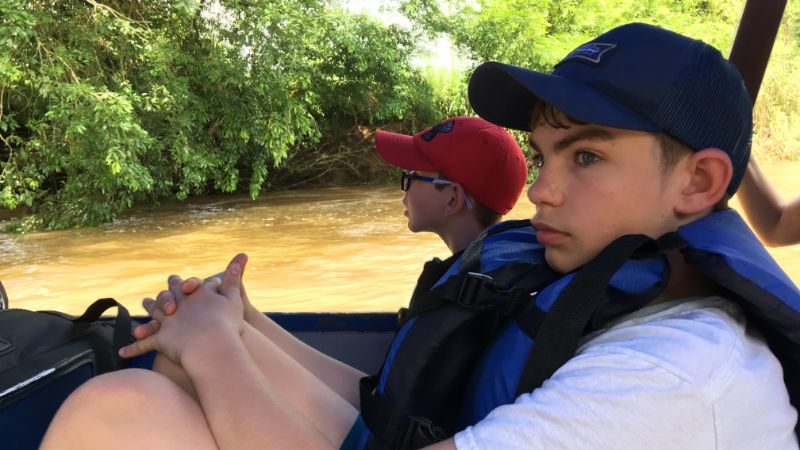 Two boys on a boat on a river.