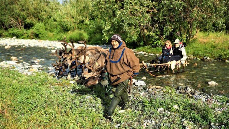 A local man and two reindeer crossing a stream in Siberia